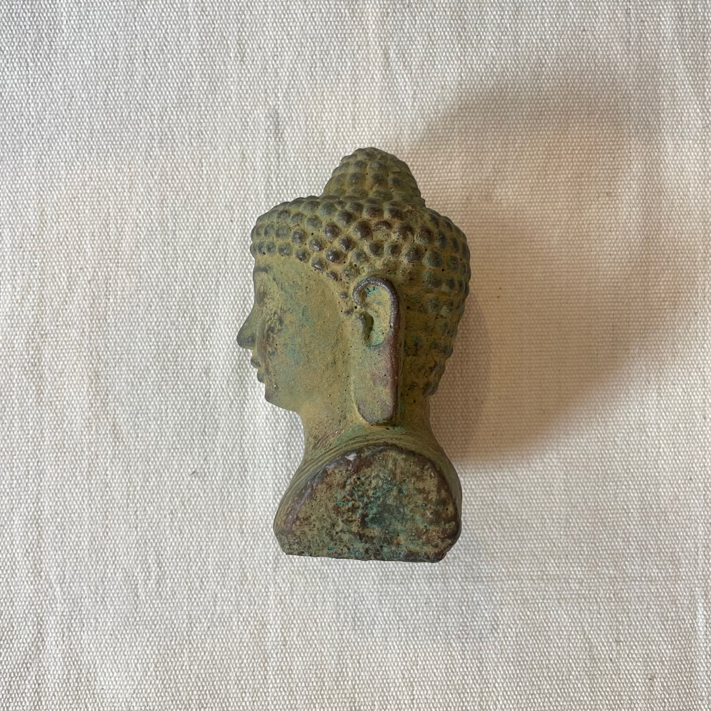 Side view of small Buddha head statue with calm expression and natural green hue