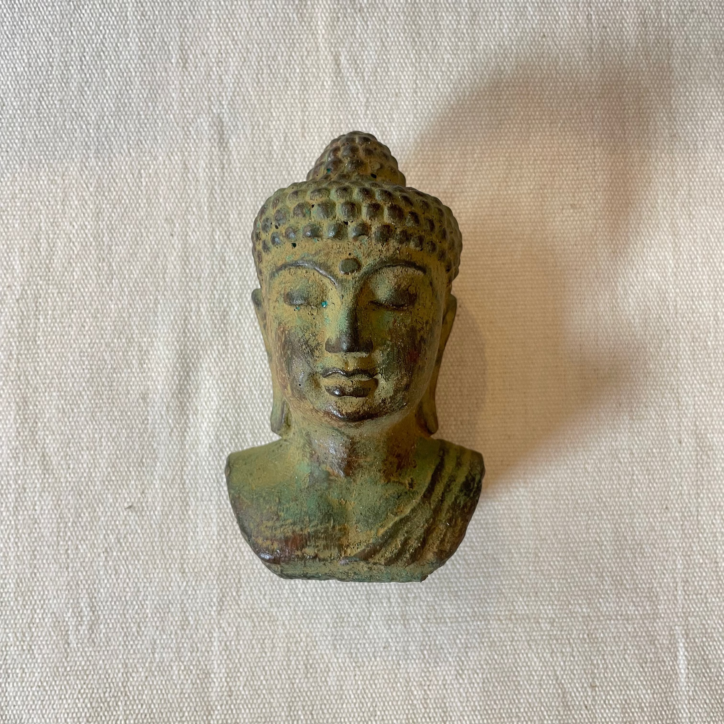 Cast sandstone Buddha head ornament with soft green finish, on linen background, hand-crafted in Bali