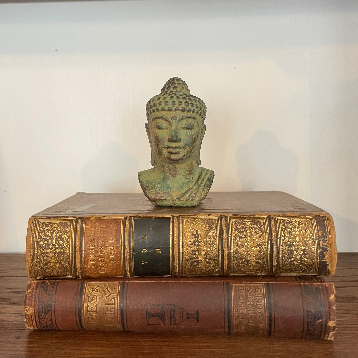 Green-toned Buddha head sculpture styled on wooden shelf beside books