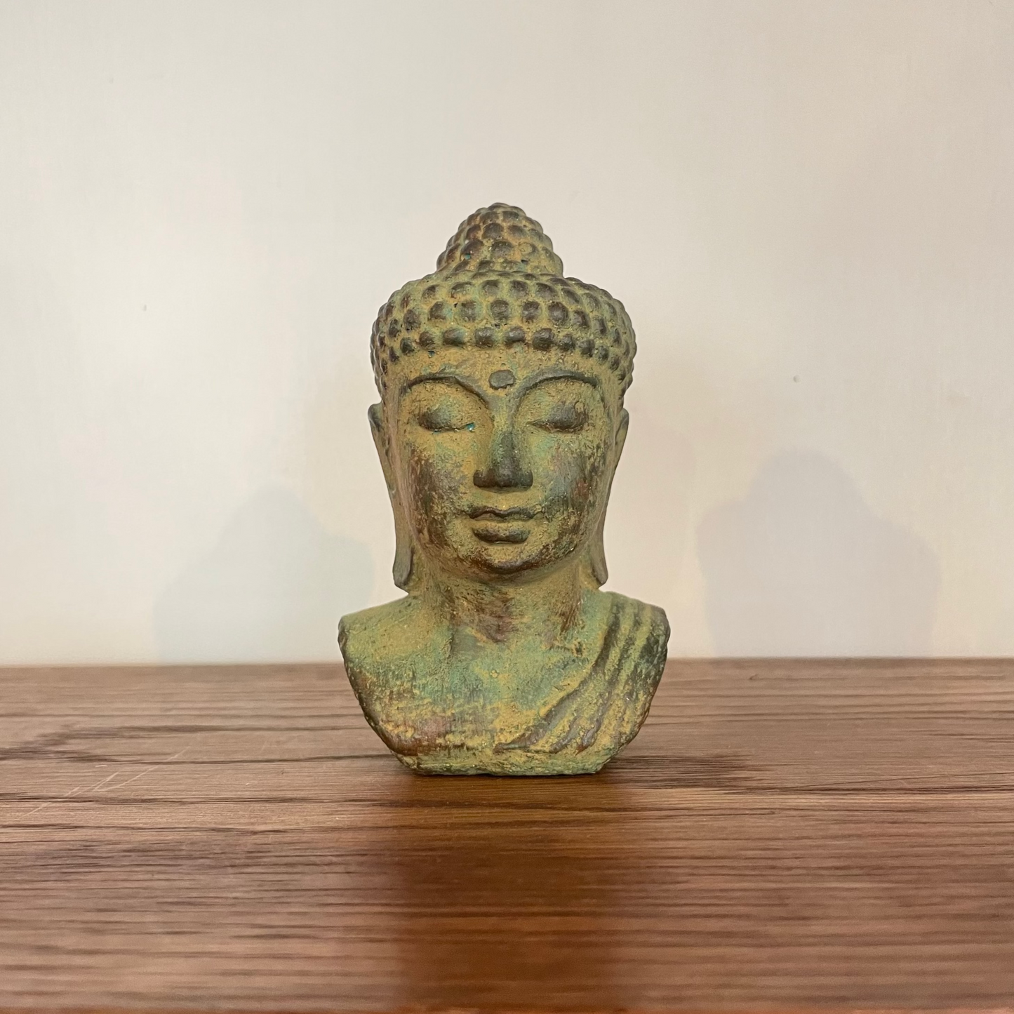Green-toned Buddha head sculpture styled on wooden shelf