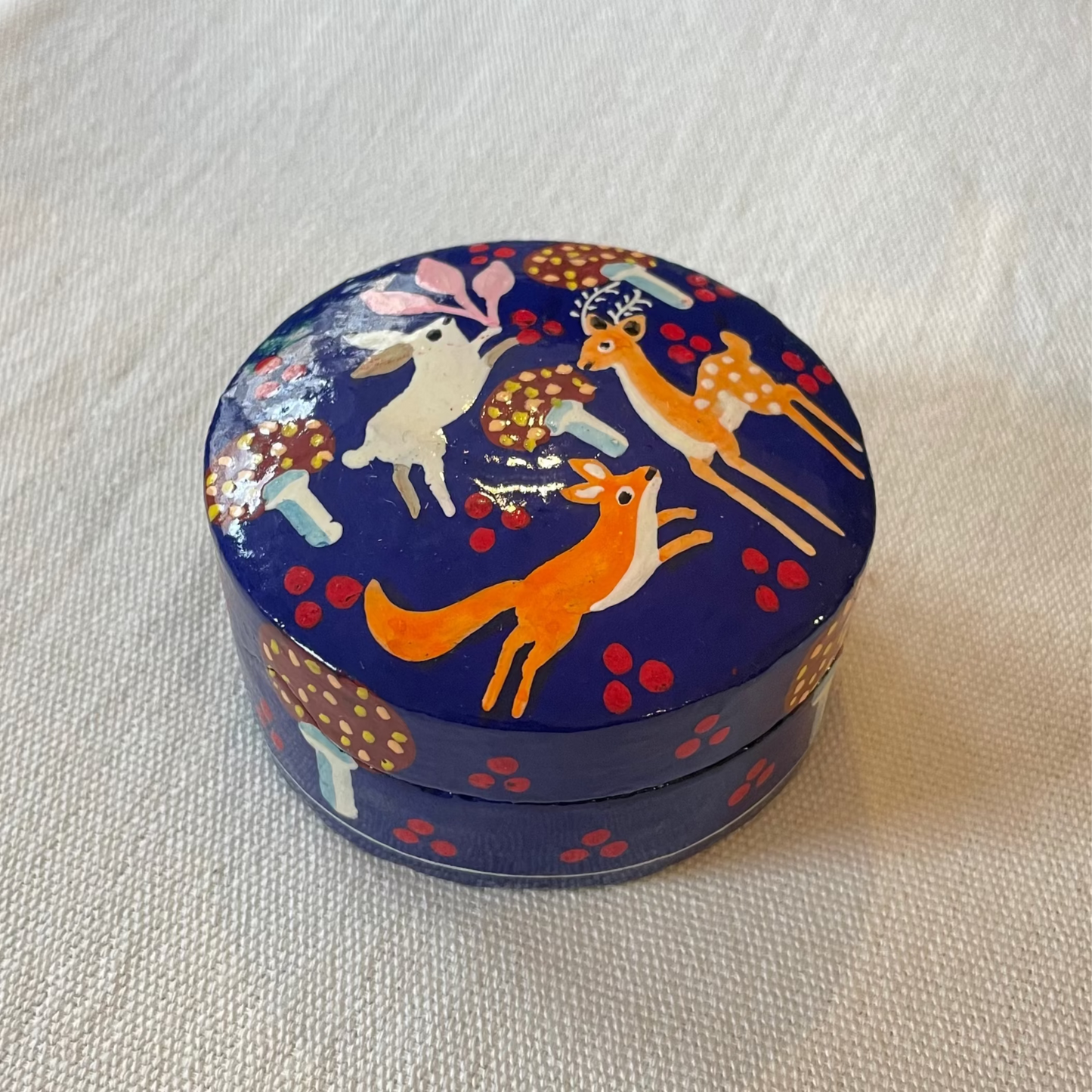 Hand-painted blue papier-mâché trinket box with woodland design on plain linen backdrop