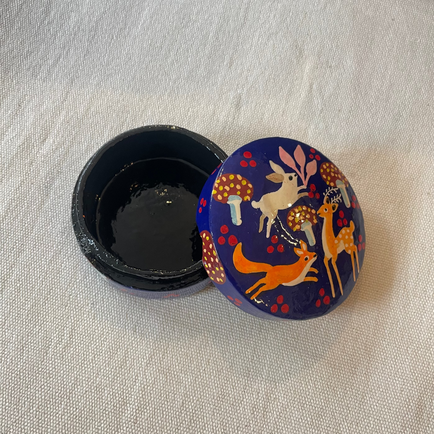 Glossy lacquered jewellery box with hand-painted woodland motif, displayed on linen cloth
