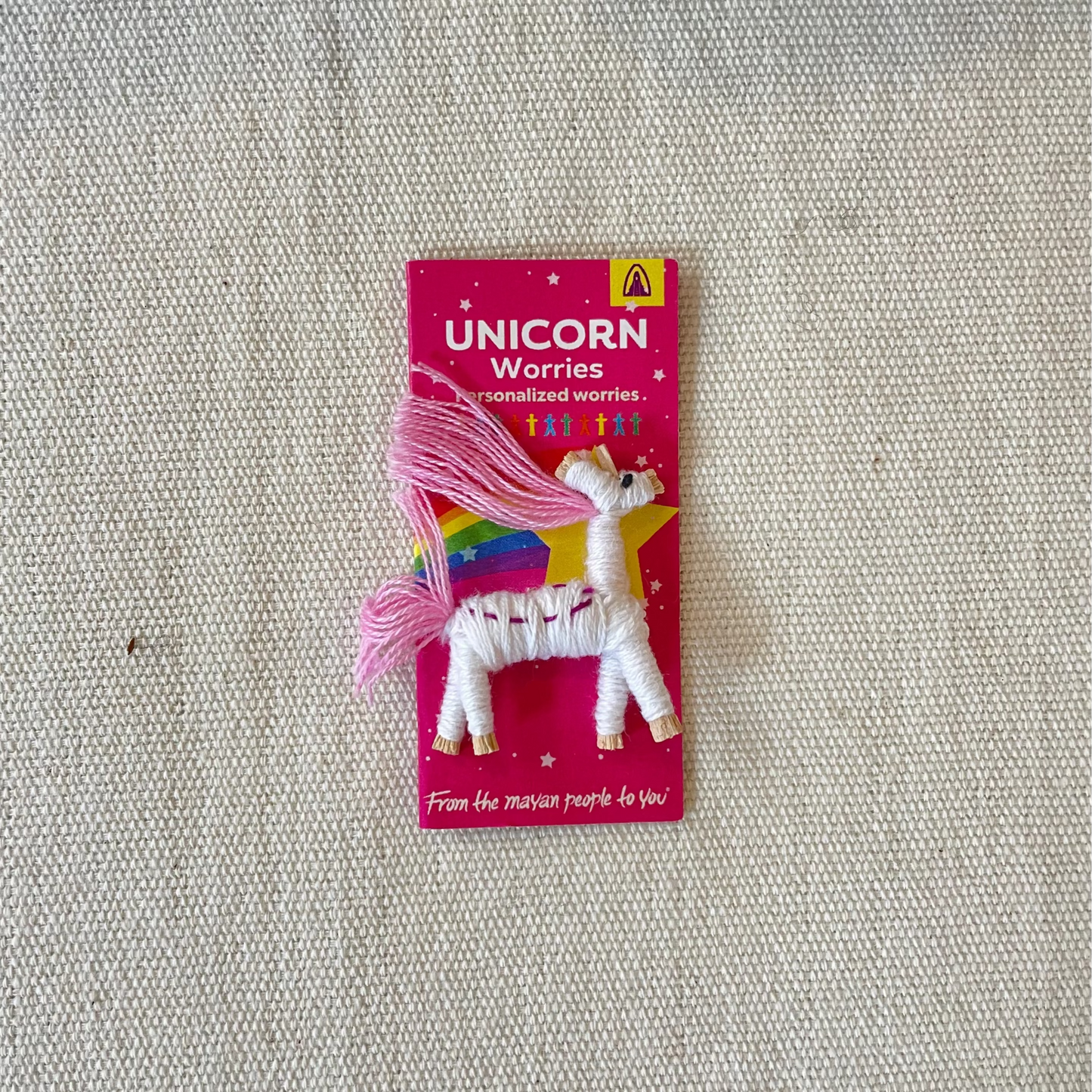 Unicorn Worry doll toy with pink hair on a neutral textured background