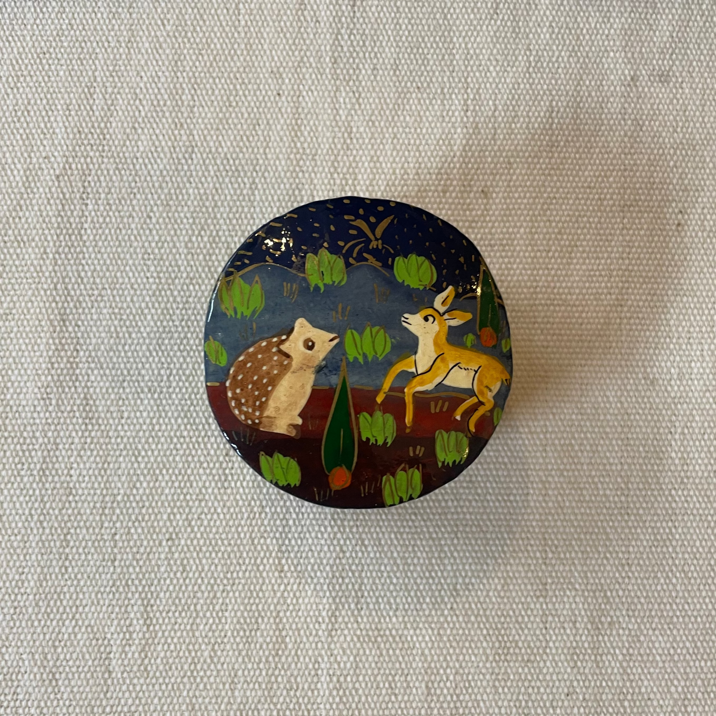 Round wooden box with animal illustrations on a textured fabric background