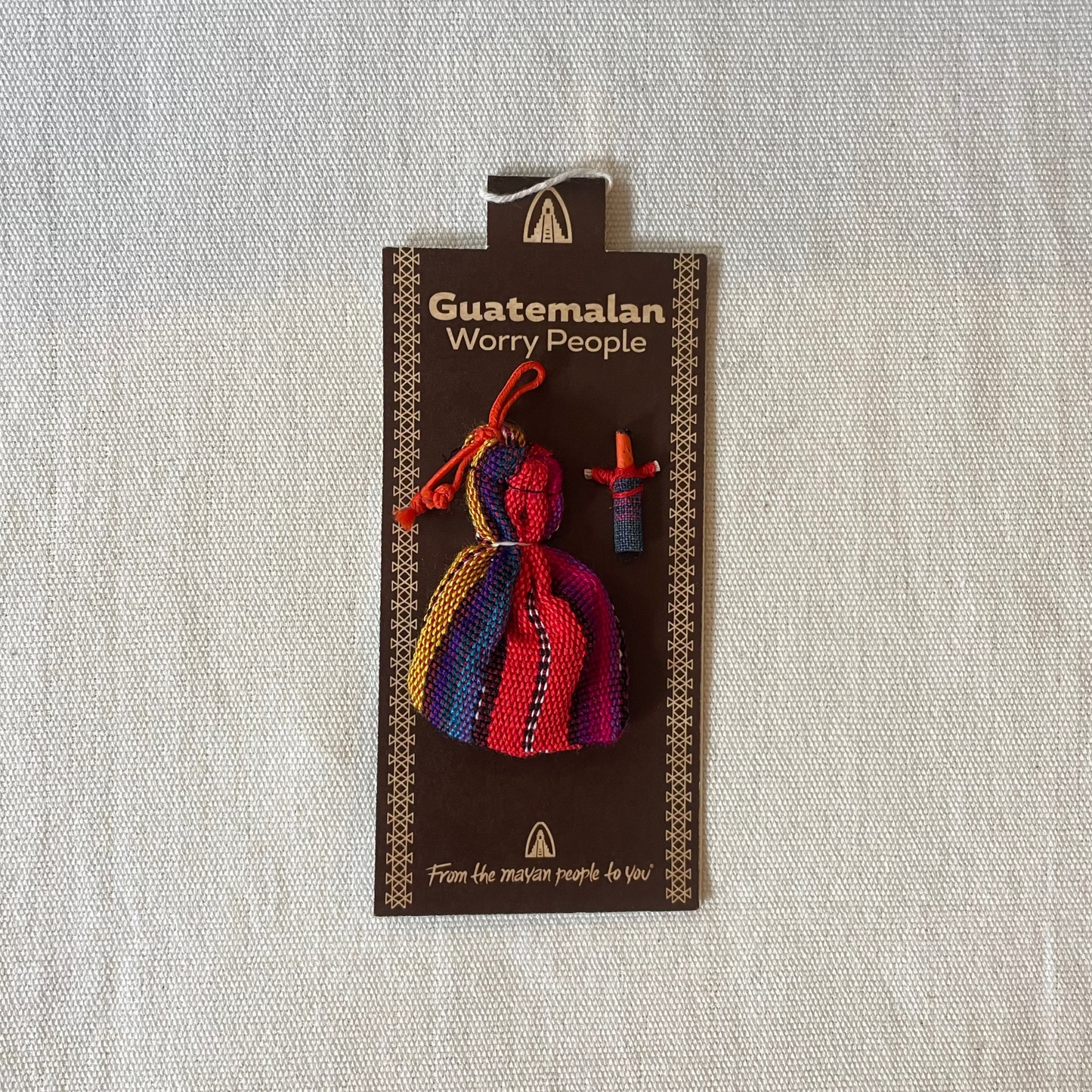 Assorted colour worry dolls for placing under pillow, shown on plain linen background