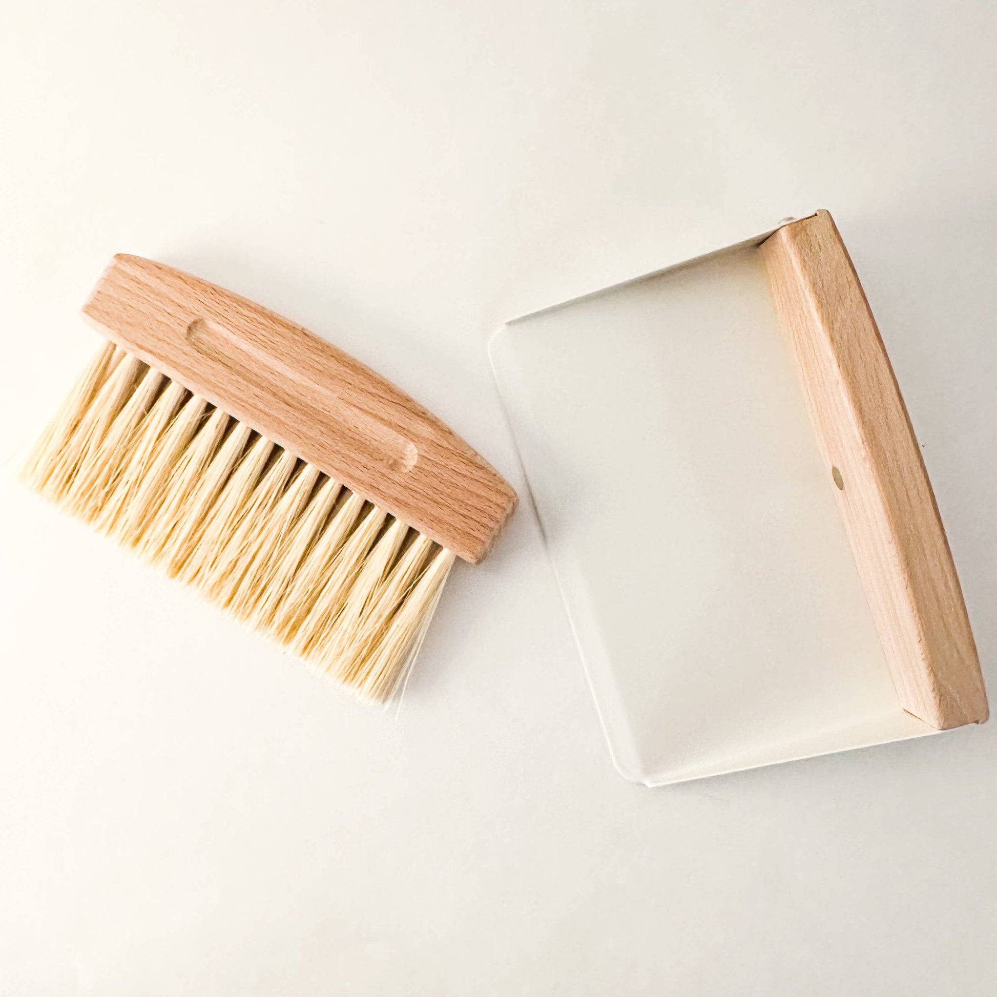 Mini beechwood broom and metal dustpan set on linen background